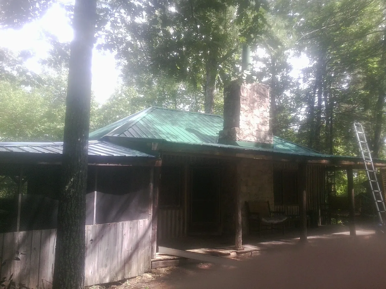 Green metal roof and stone chimney above a log cabin porch in Woodbury